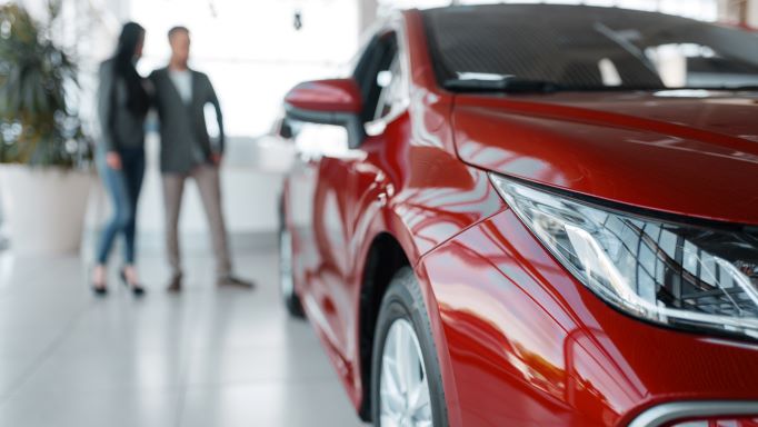 Red car in foreground, woman and man standing in the background