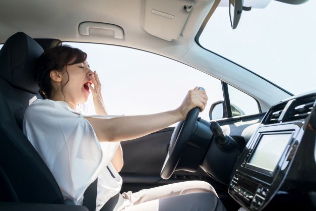 Woman yawning behind wheel of car