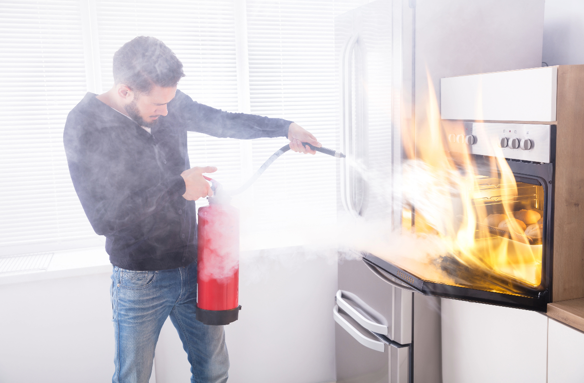 Man using a fire extinguisher on an oven fire
