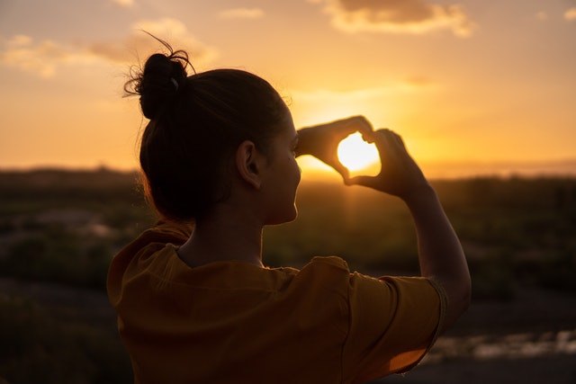 Woman making heart with hands at sunset