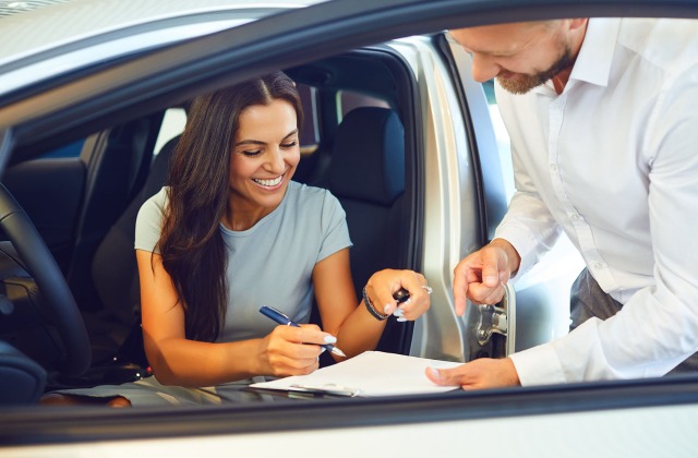 Women signing rental car agreement while sitting in car.