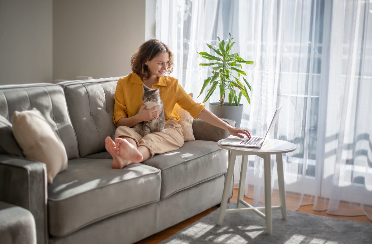 Women sitting on couch with cat looking up Renters Insurance information on computer