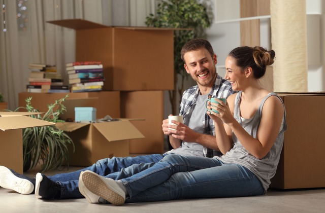 Young couple sitting on apartment floor with moving boxes. R
